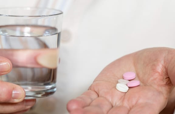 Close up of hands holding a glass of water and some pills